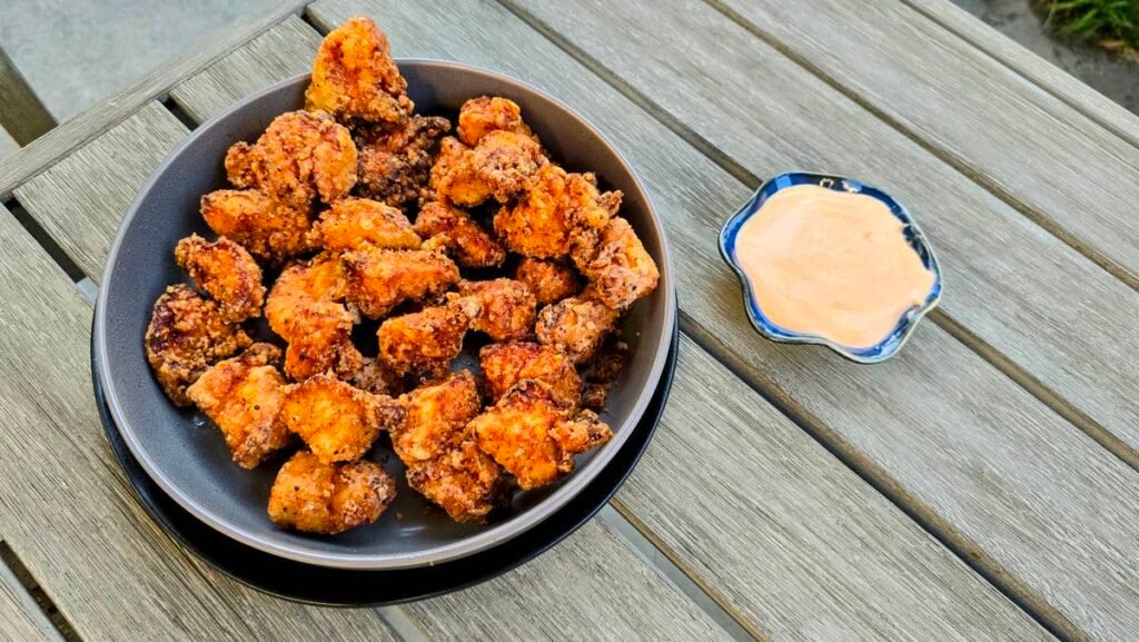 Crispy fried chicken pieces in a black bowl served with a side of dipping sauce on a wooden table.