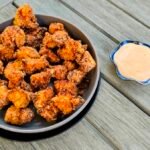 Crispy fried chicken pieces in a black bowl served with a side of dipping sauce on a wooden table.