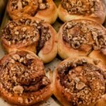 Freshly baked cinnamon rolls topped with crushed nuts in a baking tray.