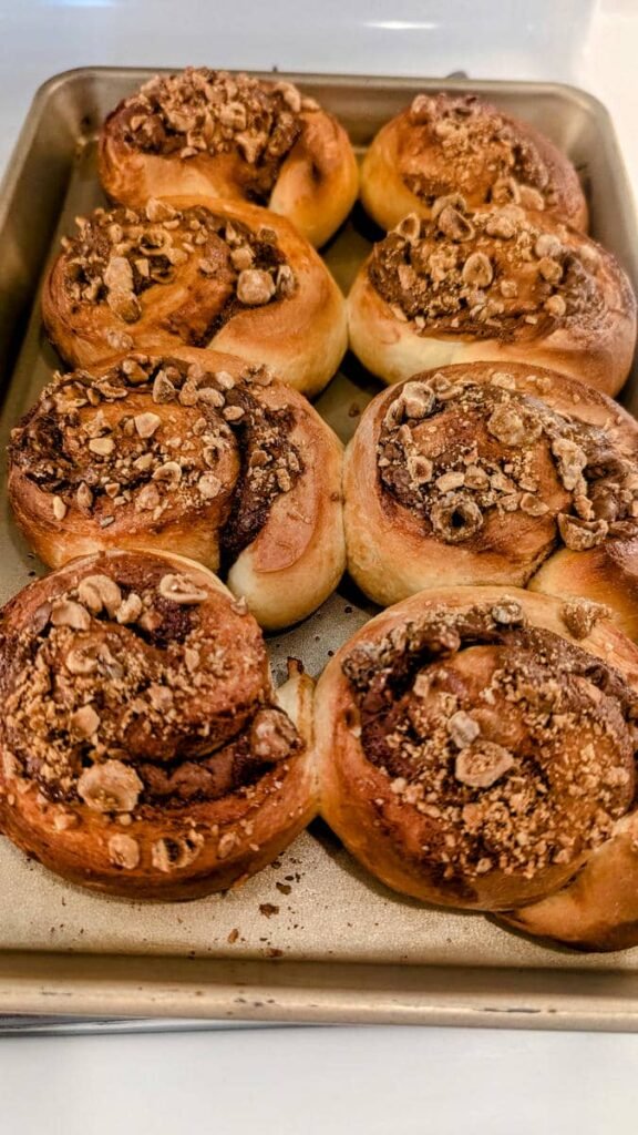 Freshly baked cinnamon rolls topped with crushed nuts in a baking tray.