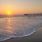 Golden sunset over the Venice Beach pier with waves crashing on the shore.