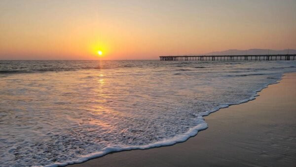 Golden sunset over the Venice Beach pier with waves crashing on the shore.